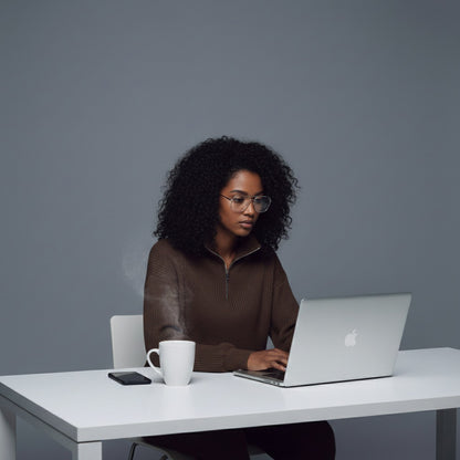 Person sitting at a desk with a laptop and a cup, against a gray background