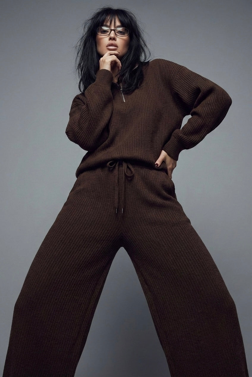 Person wearing a brown sweater and pants against a gray background
