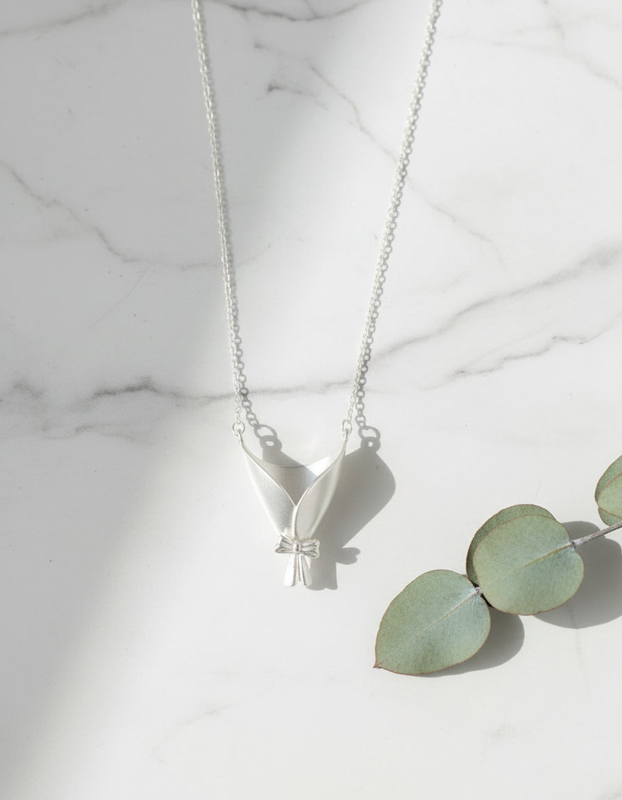 Silver necklace with a leaf pendant on a marble surface