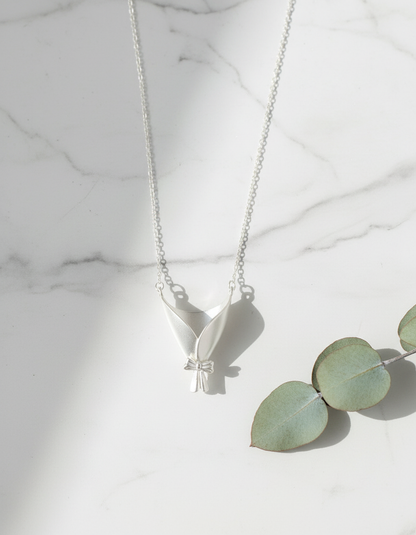 Silver necklace with a leaf pendant on a marble surface