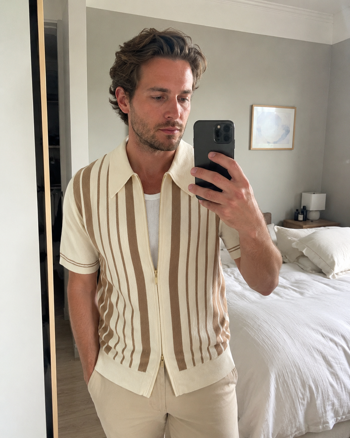 Bedroom mirror style photo of a man aged around 28 to 38 wearing the Riviera striped knit zip polo