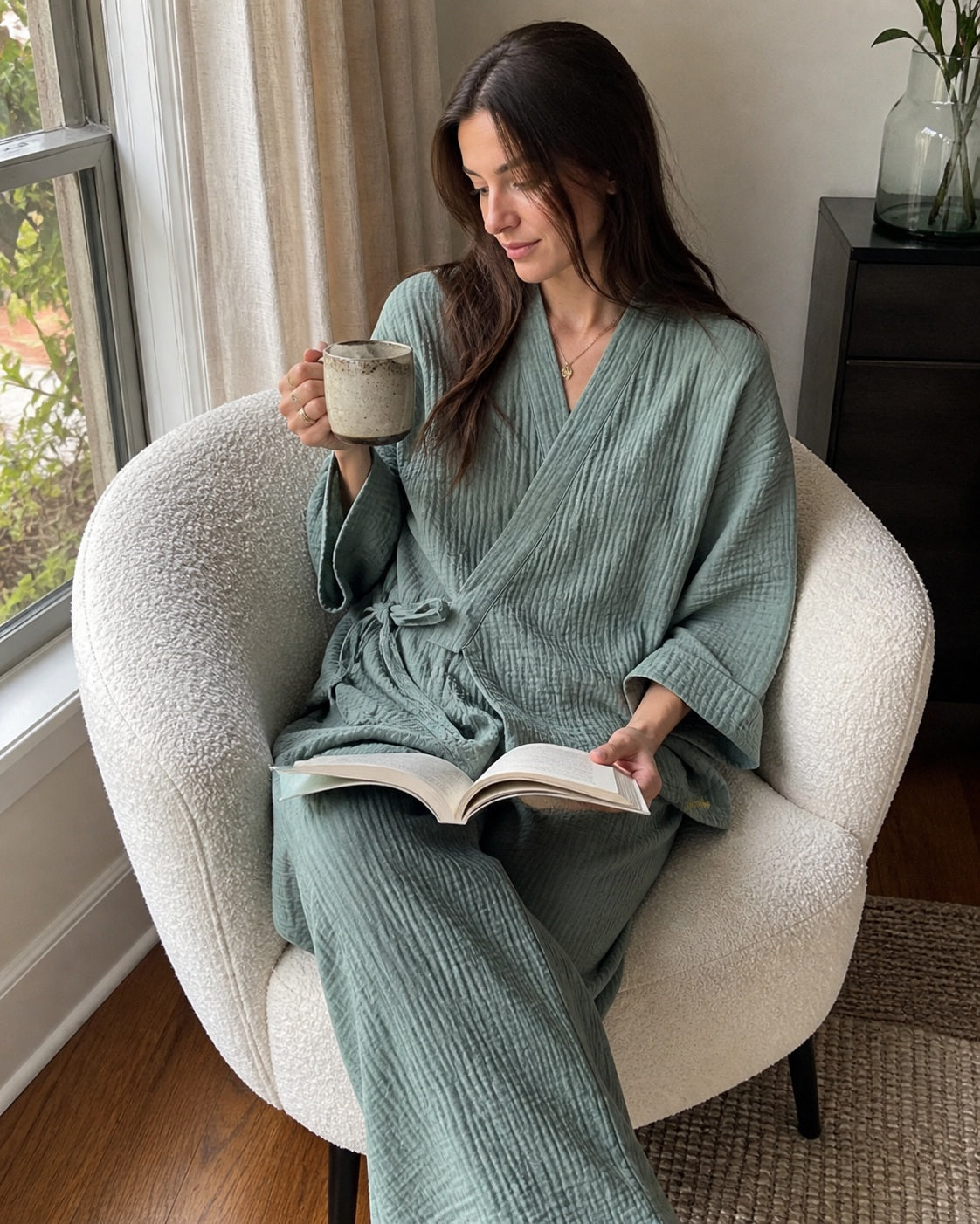 Woman wearing the sage Yoake Kimono Set while reading by a window